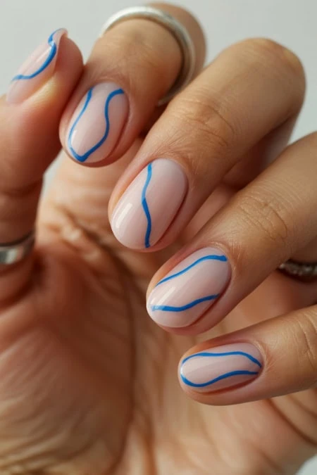 Hand showcasing modern nail art with a clear base and blue wavy lines design, perfect for a trendy and stylish look.