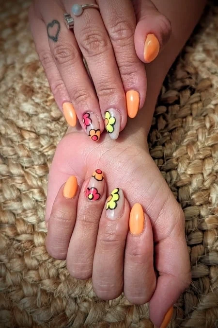 Beautiful manicured nails featuring peach polish and vibrant floral nail art with pink, yellow, and orange flowers, showcasing creative and stylish nail design on well-groomed hands.