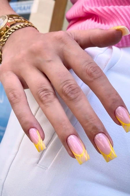 Stylish hand with yellow French manicure nails, gold bracelet, and pink clothing detail, highlighting trendy nail art, fashion accessories, and personal grooming.