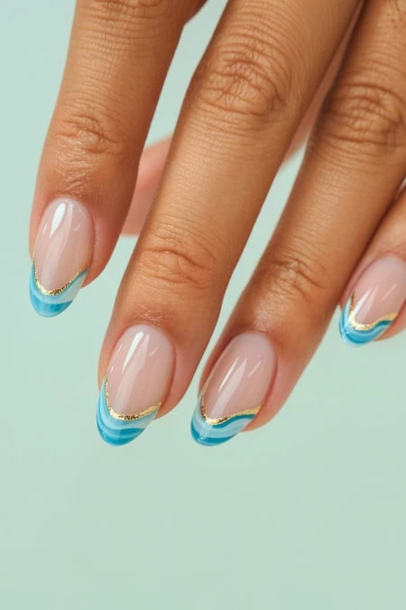 Elegant French manicure featuring natural nails with stylish blue tips and gold accents, showcasing professional nail art and beauty care.