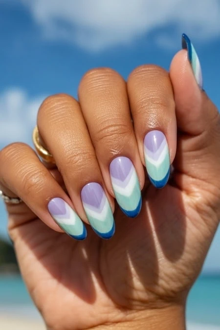 Beautiful hand with pastel chevron nail design featuring purple, blue, and mint green shades, set against a clear sky and ocean background. Perfect for summer, beach, and vacation nail inspiration.