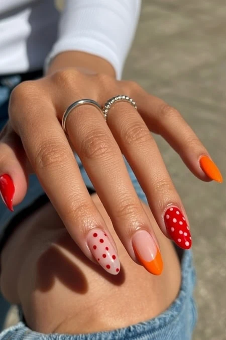 Stylish hand with vibrant polka dot and orange nail art, adorned with rings, captured outdoors with natural sunlight, emphasizing fashion and beauty accessories.