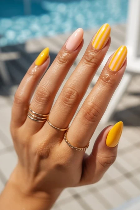 Bright yellow and pink striped manicure on well-manicured hand with gold rings, perfect for summer, poolside, and fashion accessories.