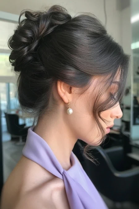Beautiful woman with an intricate, polished updo hairstyle featuring curls and twists, wearing pearl earrings and a lavender dress, in a modern salon setting. Example of beautiful prom hairstyles.
