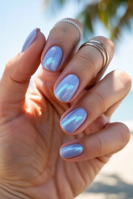 Beautiful hand showcasing blue mirror-finish manicure with multiple rings, set against a sunny beach background. Perfect for beauty, nail art, and summer fashion inspiration.