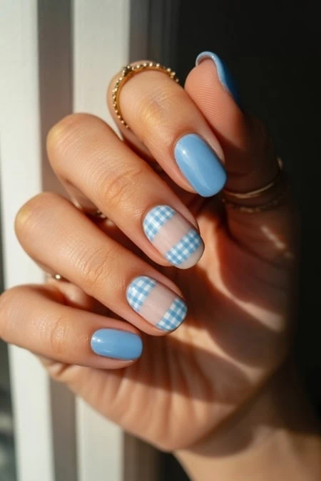 Close-up of a woman's hand with light blue manicured nails, finger touching lips, emphasizing trendy nail art and beauty care for a fresh, stylish appearance.