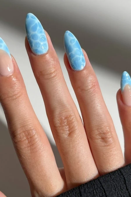Beautiful light blue watercolor nails design on well-manicured fingers, perfect for summer and spring fashion, showcasing creative and trendy nail art.
