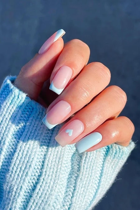 Nail art featuring a light blue French manicure with a small heart detail on the ring finger, showcasing well-groomed nails and stylish design.