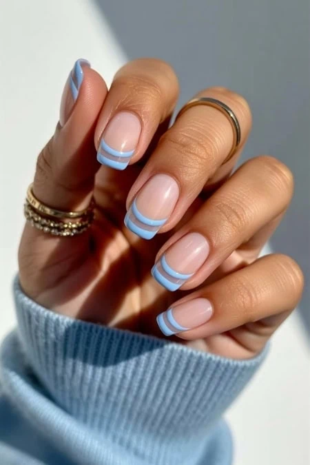 Elegant French manicure with blue accents on natural nails, showcasing stylish nail art and well-groomed hands. Perfect for beauty, nail care, and fashion-related content.