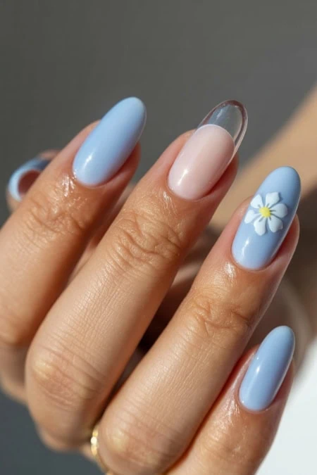 Elegant light blue nails featuring a pastel blue base with a delicate white flower accent on the ring finger, showcasing stylish and trendy nail design perfect for spring and summer.