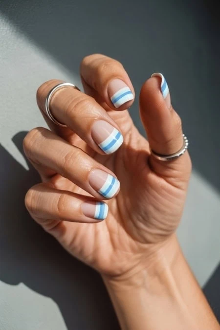 Hand with striped nail art featuring blue and white colors, adorned with rings, emphasizing beauty and self-care.
