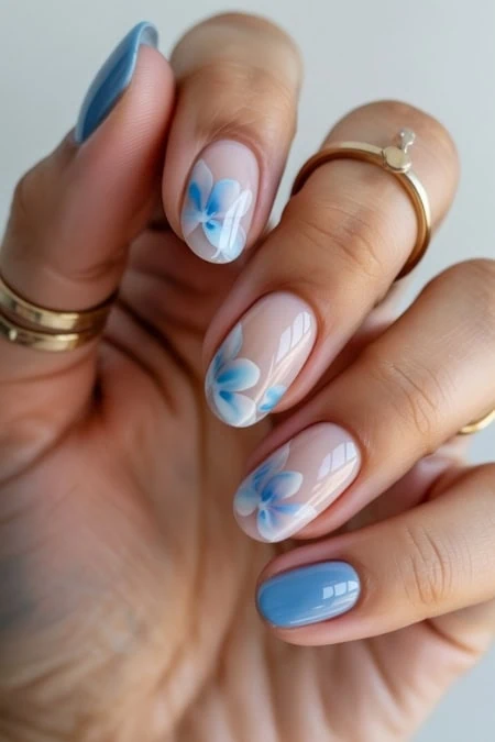 Close-up of a woman's hand with light blue manicured nails, finger touching lips, emphasizing trendy nail art and beauty care for a fresh, stylish appearance.