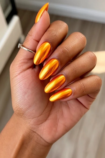 Golden metallic almond-shaped nail polish on well-manicured hand with a silver ring, showcasing trendy and luxurious nail art suitable for beauty and fashion enthusiasts.