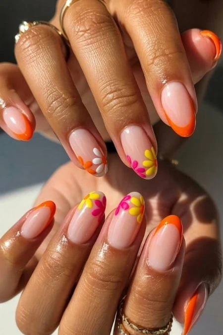 Bright floral nail art with orange, pink, yellow, and white daisy designs on natural nails, showcasing a vibrant and trendy manicure perfect for summer or spring fashion.