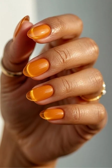 Orange gel manicure on well-manicured hand with gold rings, close-up shot emphasizing smooth, shiny nails and healthy skin, perfect for beauty, nail care, and fashion content.