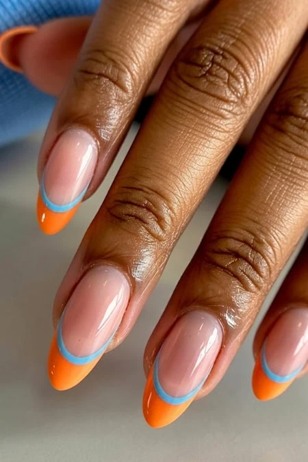 A detailed close-up of a woman's hand showcasing manicured nails with orange and blue French tips, highlighting professional nail art and healthy skin.