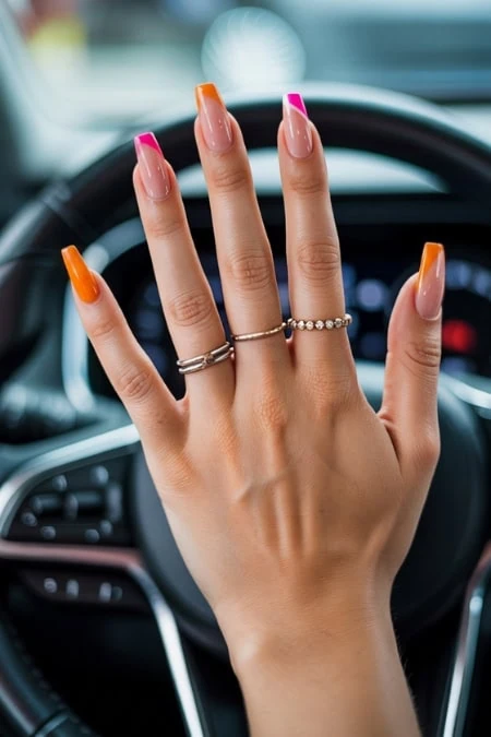Brightly colored manicured hand resting on a car steering wheel, showcasing vibrant nail polish shades for a stylish, modern look.