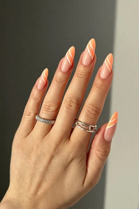A detailed description of a well-manicured hand showcasing peach-colored nails with white diagonal stripes, adorned with elegant silver rings, set against a neutral background.