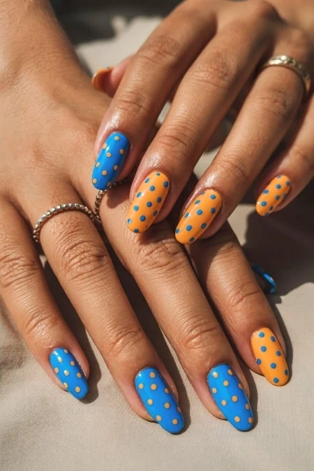 Blue and orange polka dot manicured nails on hands with rings, showcasing vibrant nail art design. Perfect for beauty, manicure, and nail art enthusiasts, emphasizing colorful, trendy nail styles.