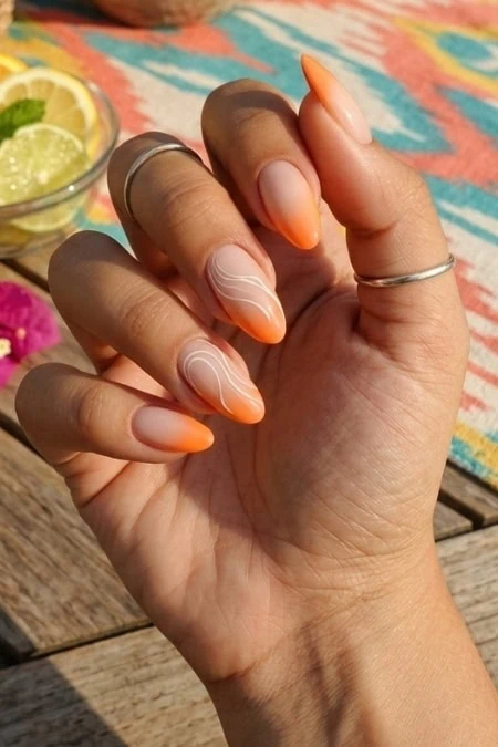 Elegant hand with orange and white marbled manicure and a colorful background featuring a wooden surface and a bowl of lemon slices, showcasing trendy and creative manicure design.