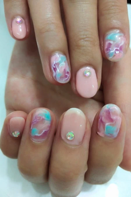 Elegant pastel marbled nail art with rhinestone accents on manicured nails, showcasing a soft pink base and colorful swirls, perfect for a stylish and sophisticated look.
