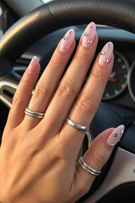 A beautiful hand with manicured nails featuring pastel pink polish and sparkling rhinestones, resting on a car steering wheel. Perfect for beauty, nail art, and fashion enthusiasts.
