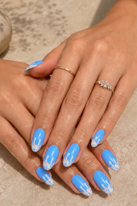 Bright blue nail polish with white floral accents on manicured nails, showcasing elegant hand jewelry, on a textured beige surface, emphasizing beauty, nail art, and personal care.
