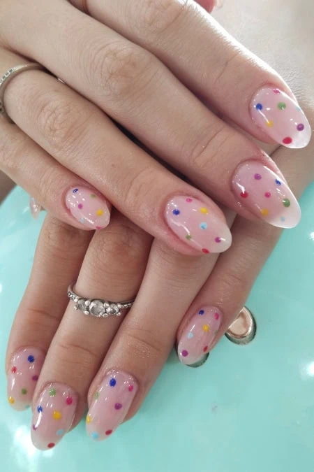 A colorful, polka dot nail art design on well-manicured hands with rings, featuring a playful and vibrant style perfect for beauty and fashion enthusiasts.