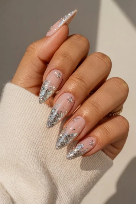 A beautiful hand with long, almond-shaped nails decorated with silver glitter and star-shaped accents, showcasing elegant nail art and well-manicured fingers.