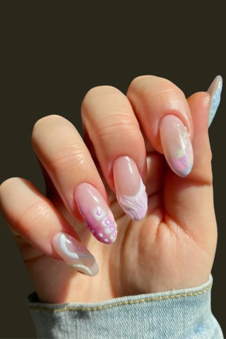 A detailed close-up of a hand with beautifully manicured nails featuring pastel marble and dot art designs, showcasing creative nail art and beauty care.