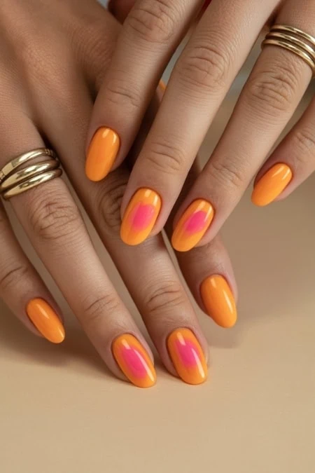 Bright orange and pink gradient manicure on well-manicured hands with gold rings, showcasing trendy nail art and vibrant summer style.