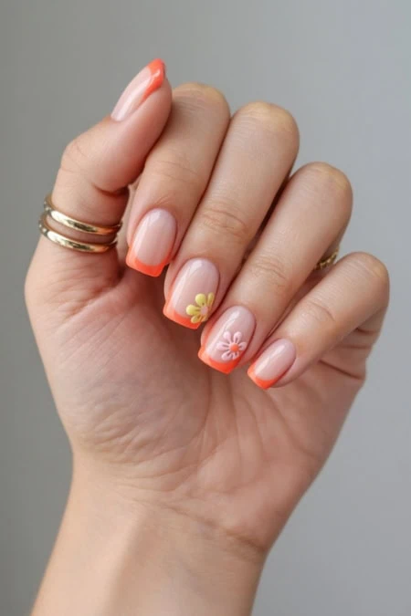 A beautiful hand with manicured nails featuring a natural pink base and vibrant orange tips, decorated with delicate yellow and white floral nail art, showcasing elegant nail design and grooming.