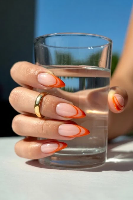 A woman’s hand with manicured nails holding a glass of water outdoors, emphasizing hydration and beauty care.