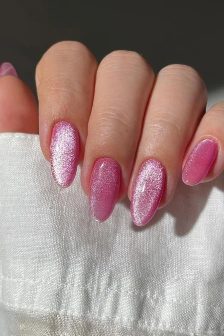 A detailed close-up of a hand with manicured nails painted in shimmering pink nail polish, showcasing well-groomed cuticles and smooth skin, against a neutral background.