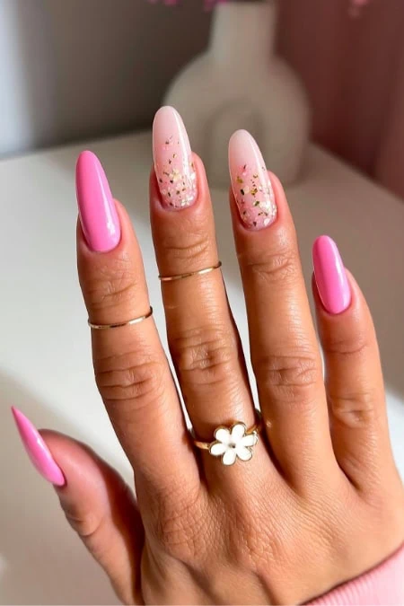 Bright pink and glittery nail art on well-manicured fingers, featuring a daisy ring, showcasing trendy, stylish, and vibrant nail design perfect for beauty and fashion enthusiasts.