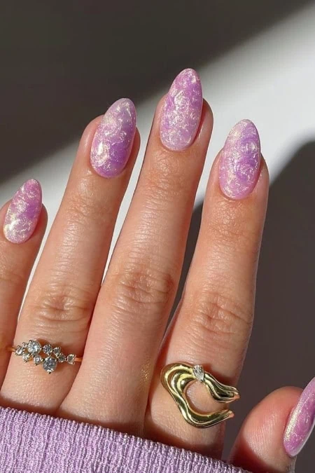 A beautiful hand with lavender marble nail polish and gold and silver rings, showcasing elegant and trendy manicure and jewelry for a stylish look.