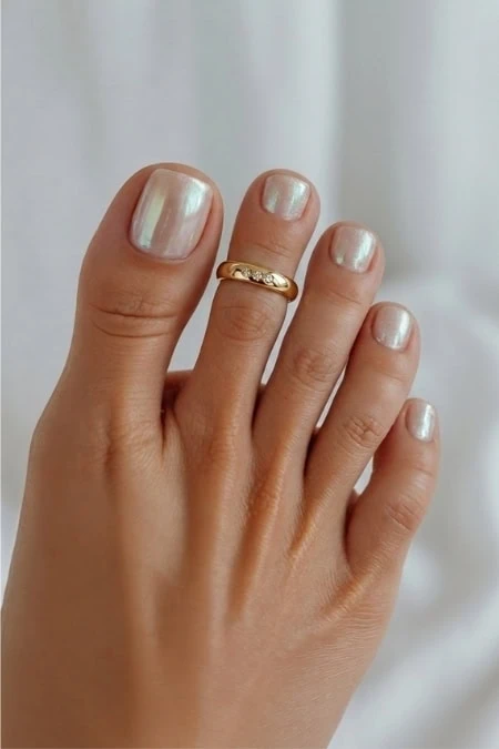 Close-up of a well-groomed hand with shiny, neutral-colored nails and a gold ring, highlighting beauty and self-care. Perfect for beauty, nail care, and jewelry themes.