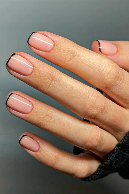 Close-up of a hand with neatly manicured nails featuring a short nail design and modern black and white French tip design on a neutral background showcasing a shirt nail design.