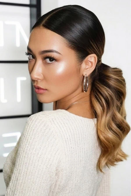 A woman with long, wavy ombre hair, wearing hoop earrings and a cream sweater, posing indoors with a modern, minimalistic background. Perfect for beauty, hair, and fashion content.
