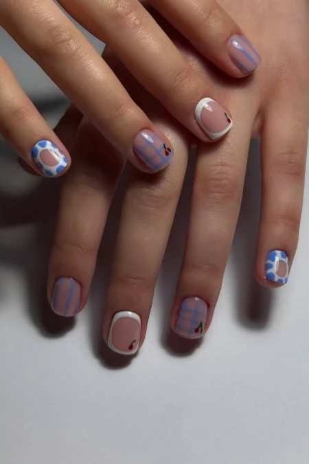 Colorful geometric nail art featuring blue, white, and beige patterns with plaid and polka dot designs on well-manicured nails.
