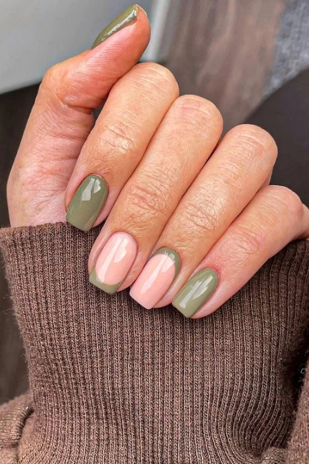 Close-up of a manicured hand with olive green and natural pink nail polish, showcasing a stylish and well-maintained manicure.