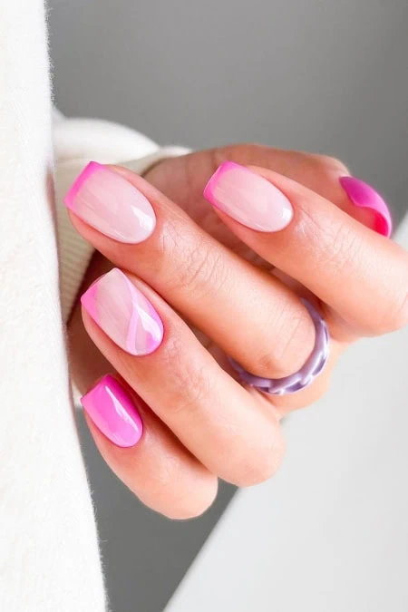 Close-up of a woman's hand with manicured nails featuring pink and white marble design, wearing a purple ring, against a neutral background.