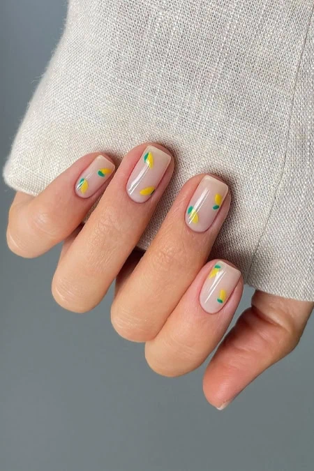 Close-up of a hand with manicured nails featuring pastel yellow, blue, and white geometric nail art on a neutral background.