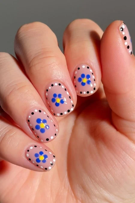 Colorful floral nail art with blue and yellow flowers and black dotted accents on natural nails, perfect for spring or summer fashion.