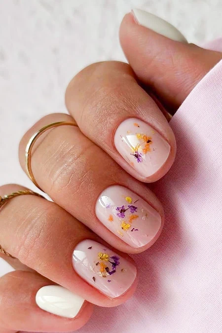 Elegant manicure with white base and colorful floral nail art featuring purple, yellow, and orange accents, perfect for spring or summer beauty looks.