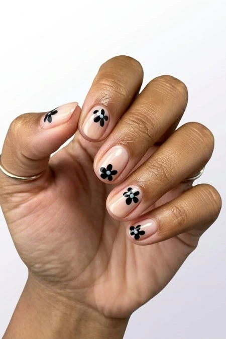 Close-up of a hand with manicure featuring black flower nail art on a neutral background.