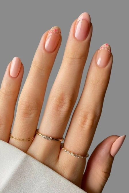 Close-up of a woman's hand with manicured nails featuring a soft pink polish and delicate floral accents, adorned with dainty gold rings.