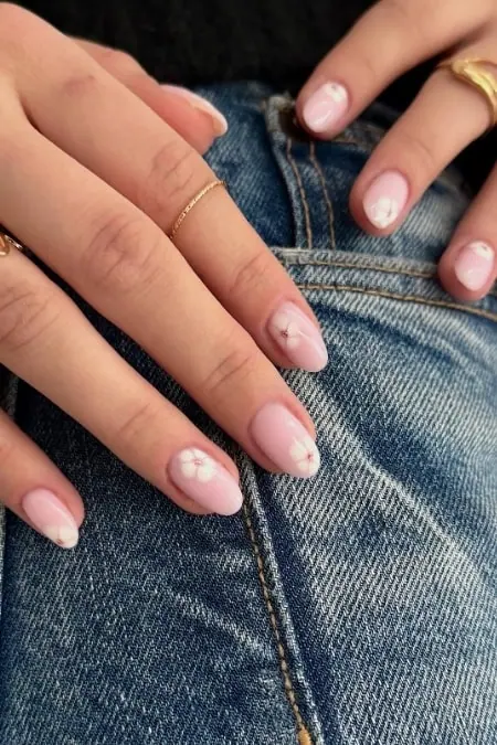 Close-up of manicured fingernails with floral nail art resting on blue denim jeans, showcasing stylish nail design and well-groomed hands.