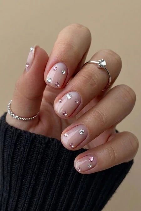 Close-up of a woman's hand with manicure decorated with small rhinestones, wearing a silver ring with a large gemstone and a delicate silver bracelet.
