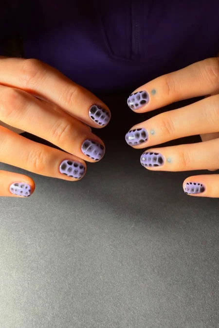 Close-up of hands with stylish purple and black polka dot nail art, showcasing creative manicure design for beauty and fashion enthusiasts.